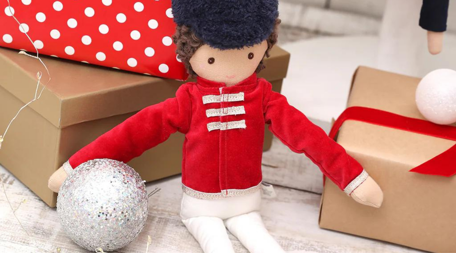 A doll of a tin soldier in a red military style jacket propped against a stack of wrapped Christmas gifts.