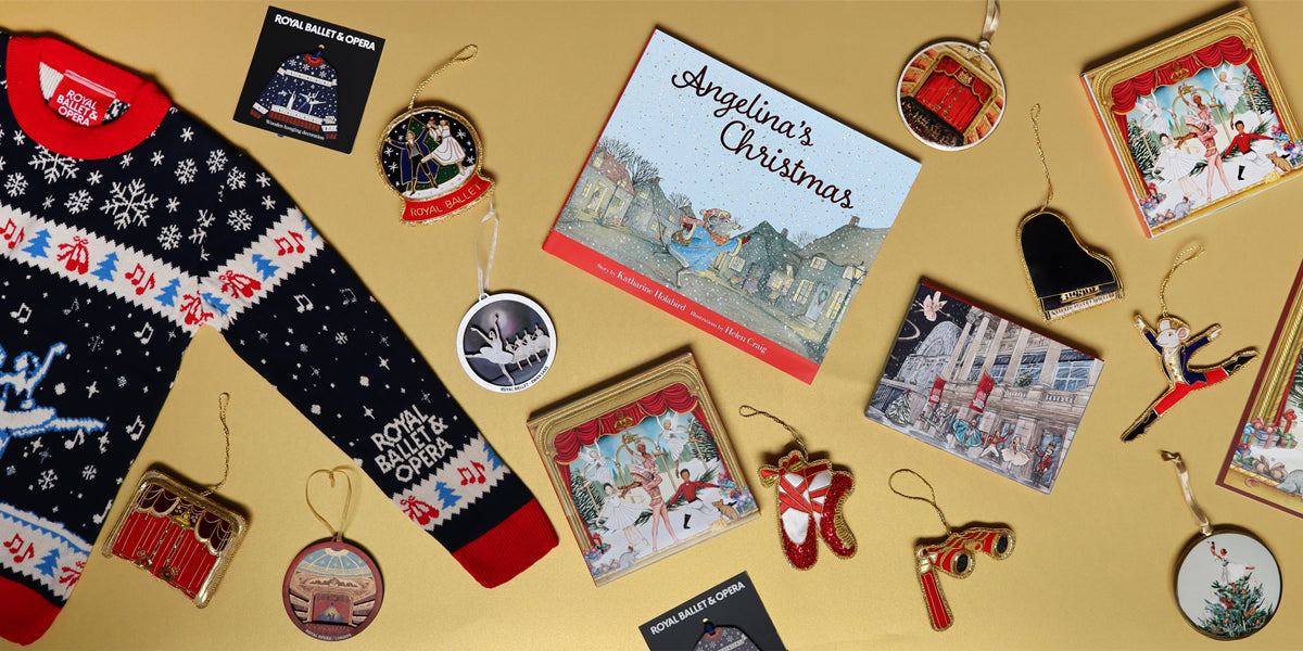 A styled flat-lay of Christmas-themed merchandise on a warm gold background, including a navy christmas jumper with red and white patterns, a children's book titled 'Angelina's Christmas', multiple illustrated decorations, and small hanging decorations.