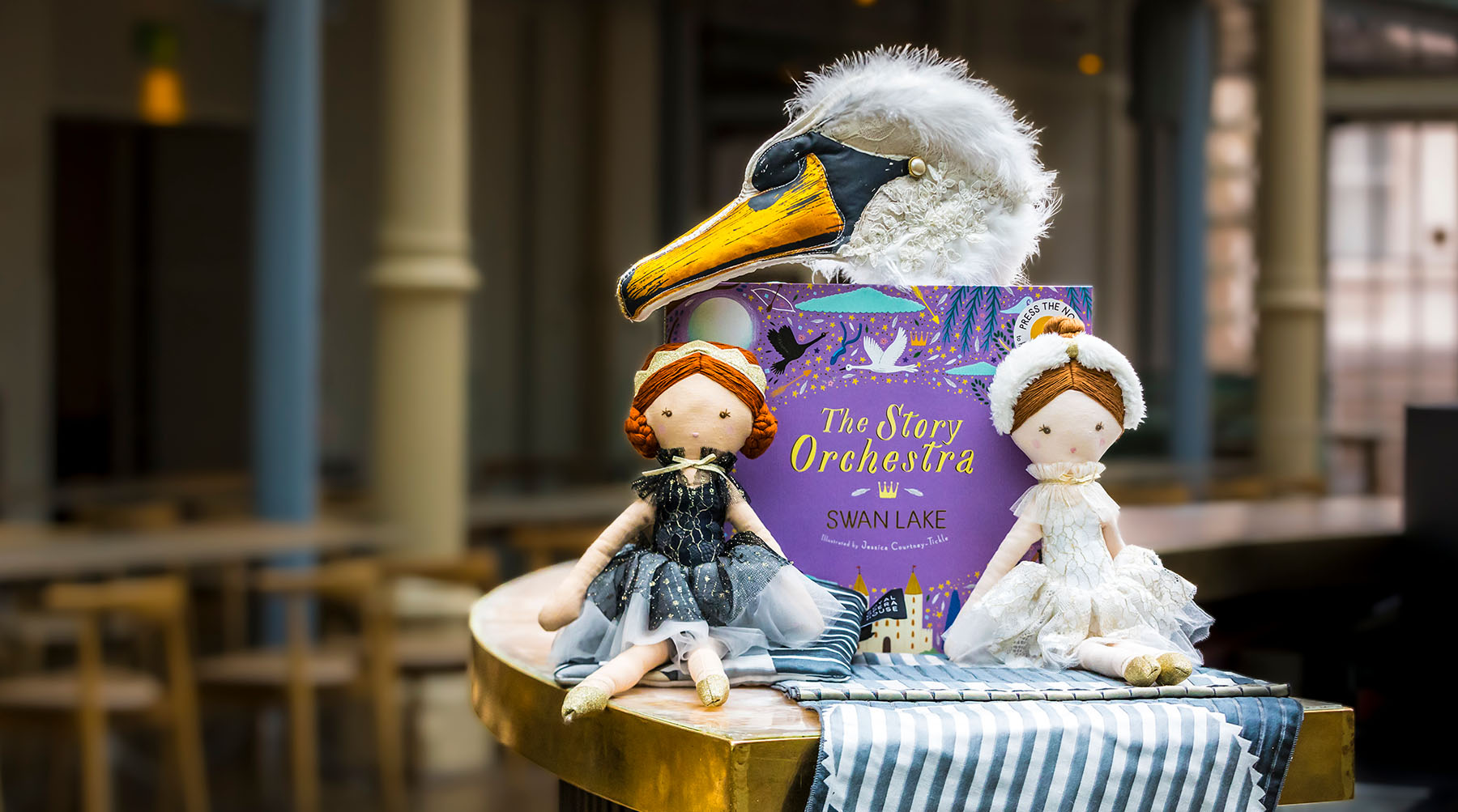 Two dolls dressed as the black and white swan sit on a round table propped up against a purple picture book.
