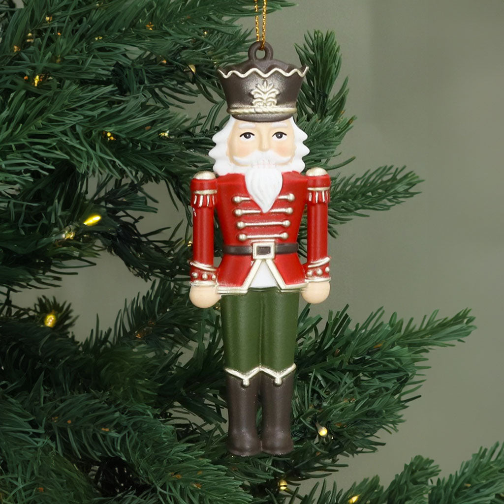 nutcracker soldier in a red and gold jacket, green trouser and black boots with a black and gold hat  hanging decoration on a christmas tree with lights