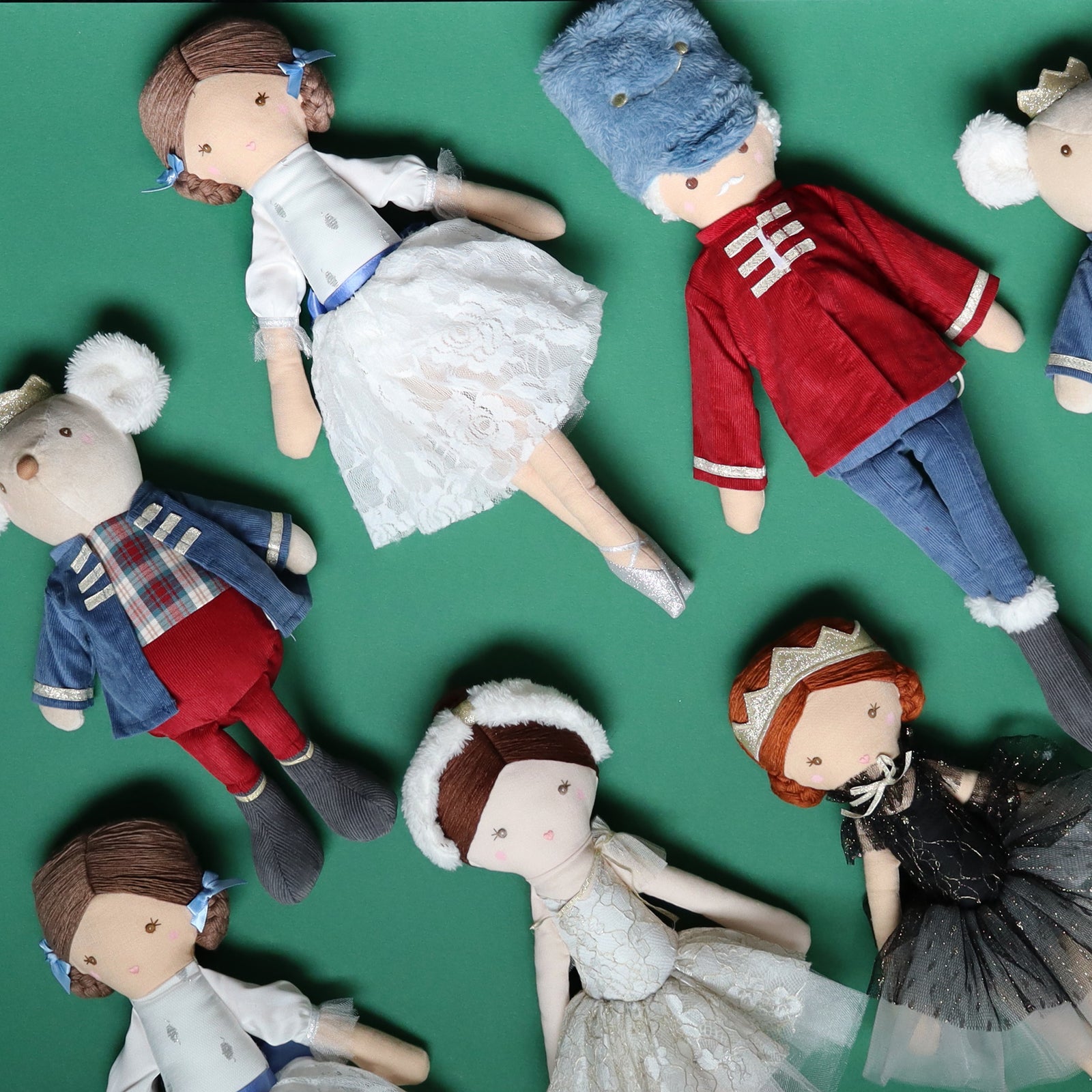 A collection of handmade ballet themed fabric dolls with embroidered faces, arranged on a solid green background.