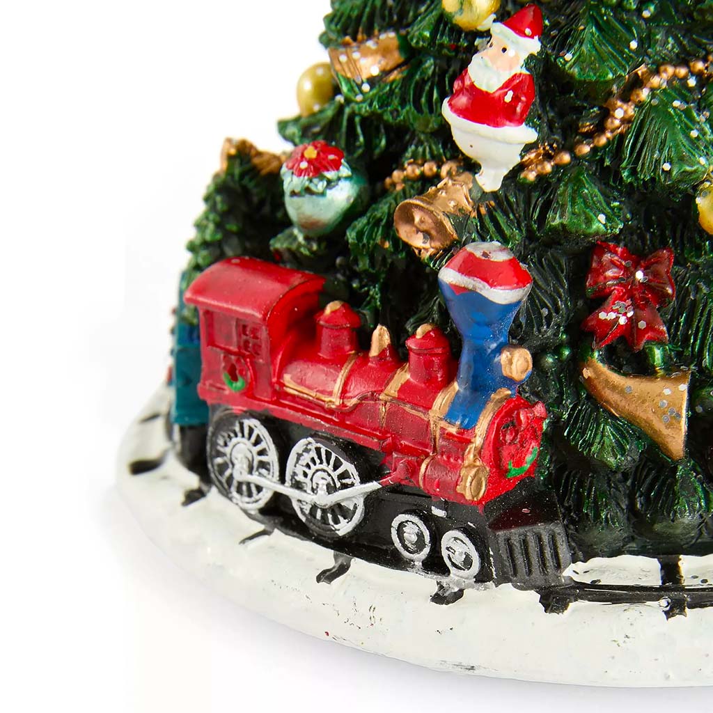 A close-up of a Christmas tree music box featuring a red and blue steam locomotive on tracks, decorated with green pine branches, gold ornaments, a Santa Claus figure, and red bows, set against a plain white background.