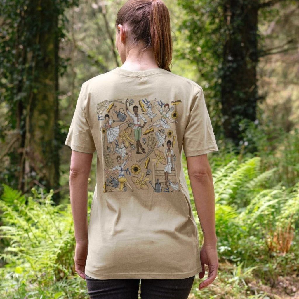 Person wearing an oat coloured t-shirt with a colourful ballet design on the back, standing in a forest.
