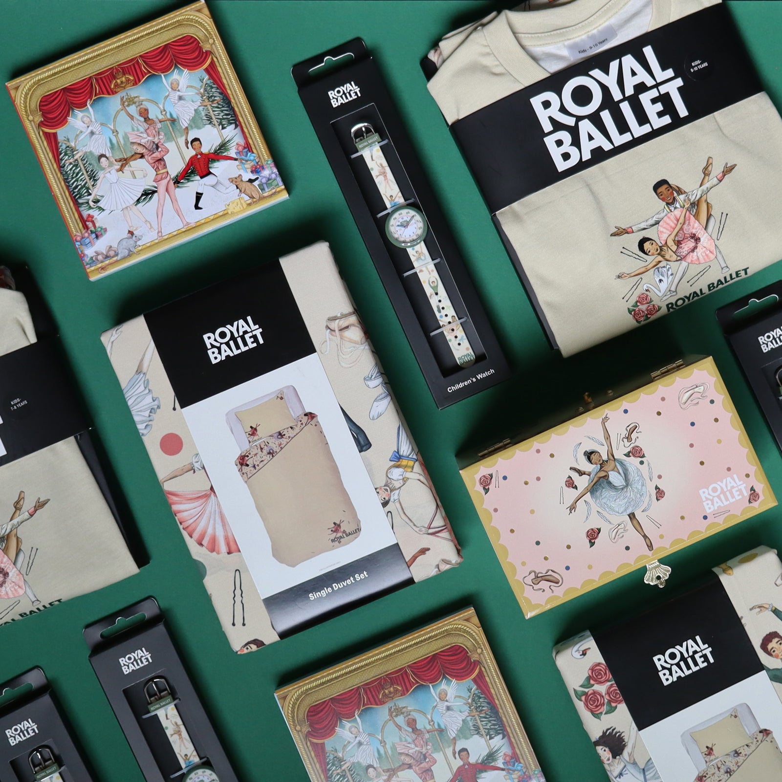 A styled flat-lay of multiple Royal Ballet-branded childrens products arranged on a dark green background, including a pjs, watch, bedding set, and jewellery box with ballet-themed illustrations.