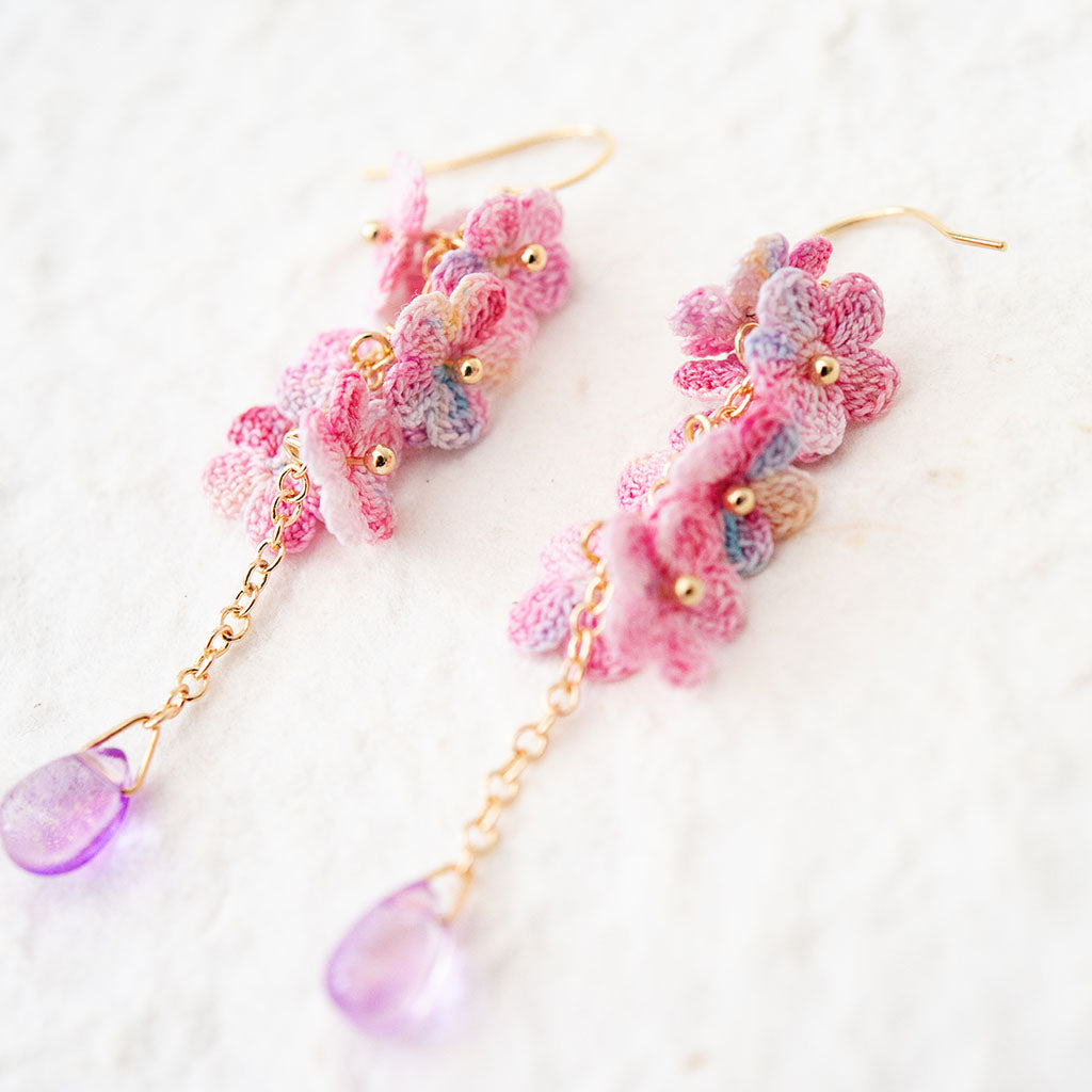gold plated drop earrings with pink micro crochet flowers and a purple bead on a white background
