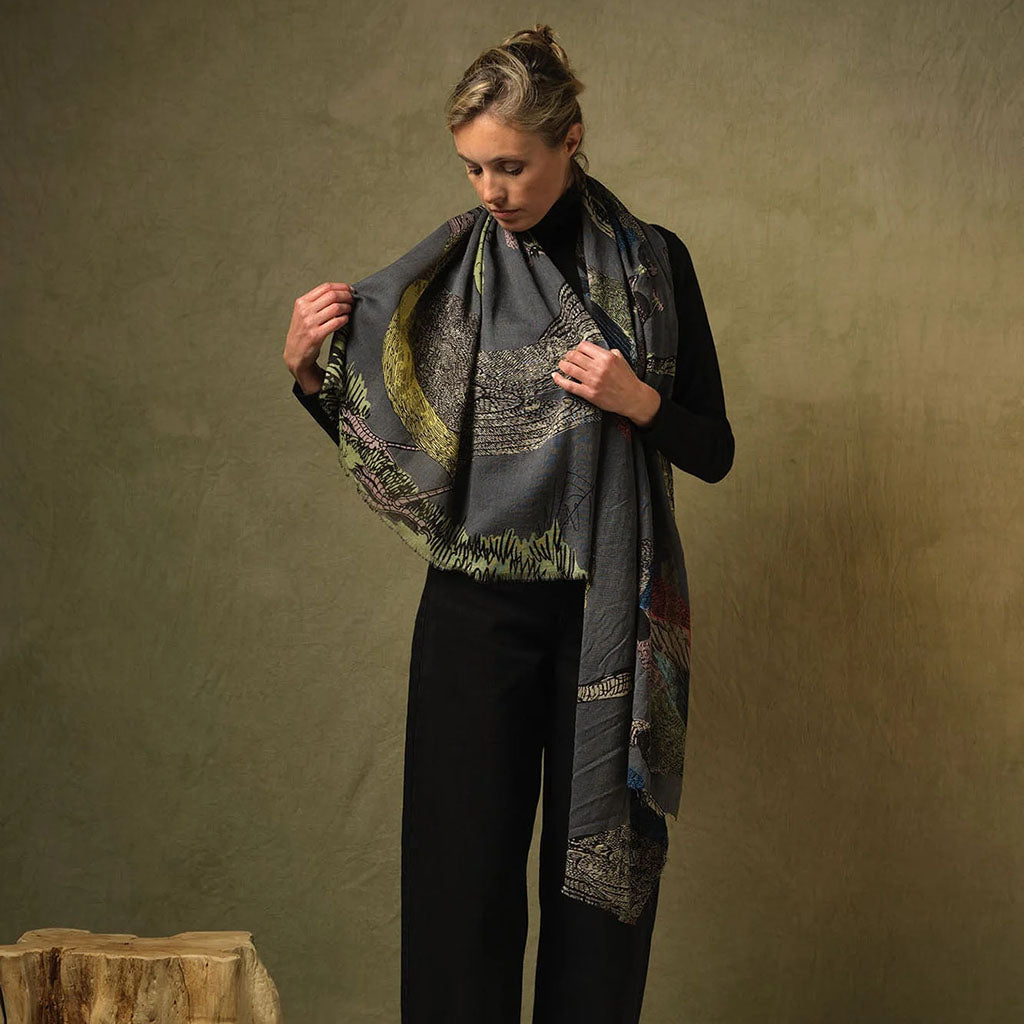 Woman holding a bird patterned scarf against a plain background