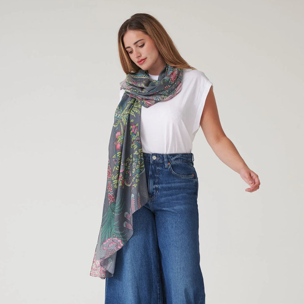 Woman wearing a floral patterned grey scarf, white shirt, and blue wide leg jeans on a plain background