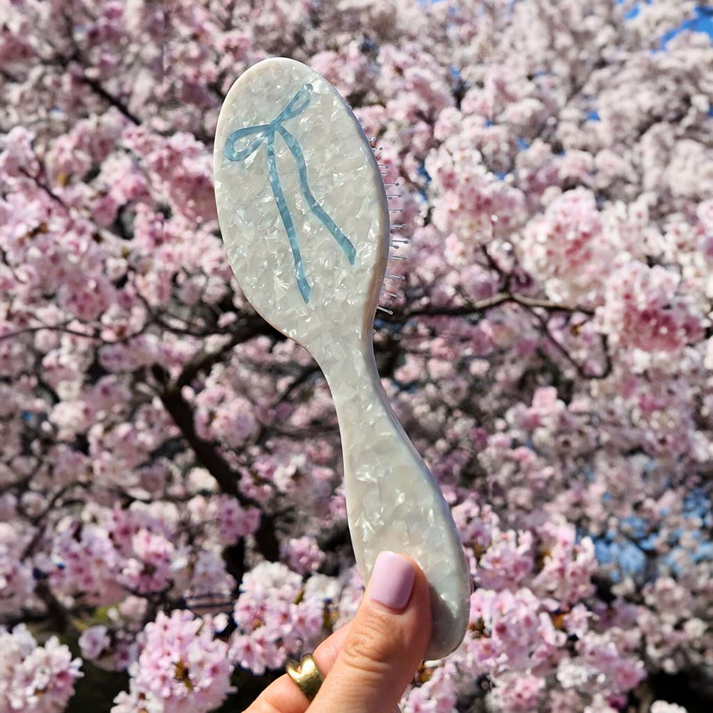 Hairbrush with a blue bow design held in front of cherry blossom trees
