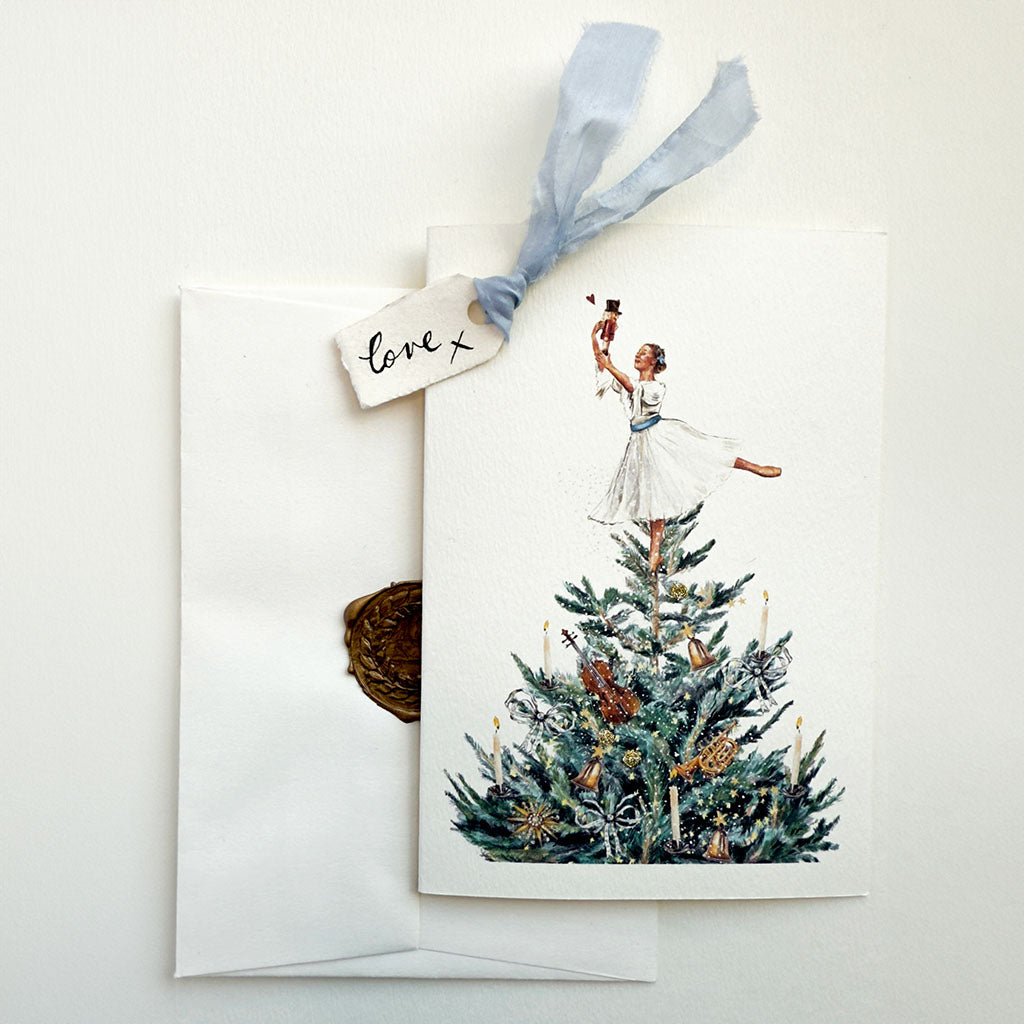 Greeting card with a Christmas tree, Clara and a nutcracker Doll illustration, tied with a ribbon, on a white background.