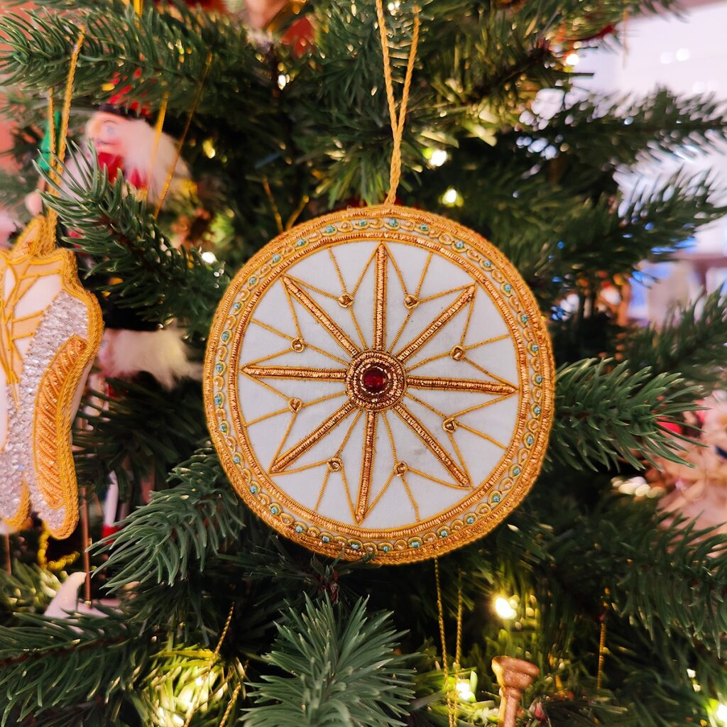 Decorative circular decoration inspired by the auditorium ceiling  at the RBO with gold  and blue detailing and a red gemstone on a white background