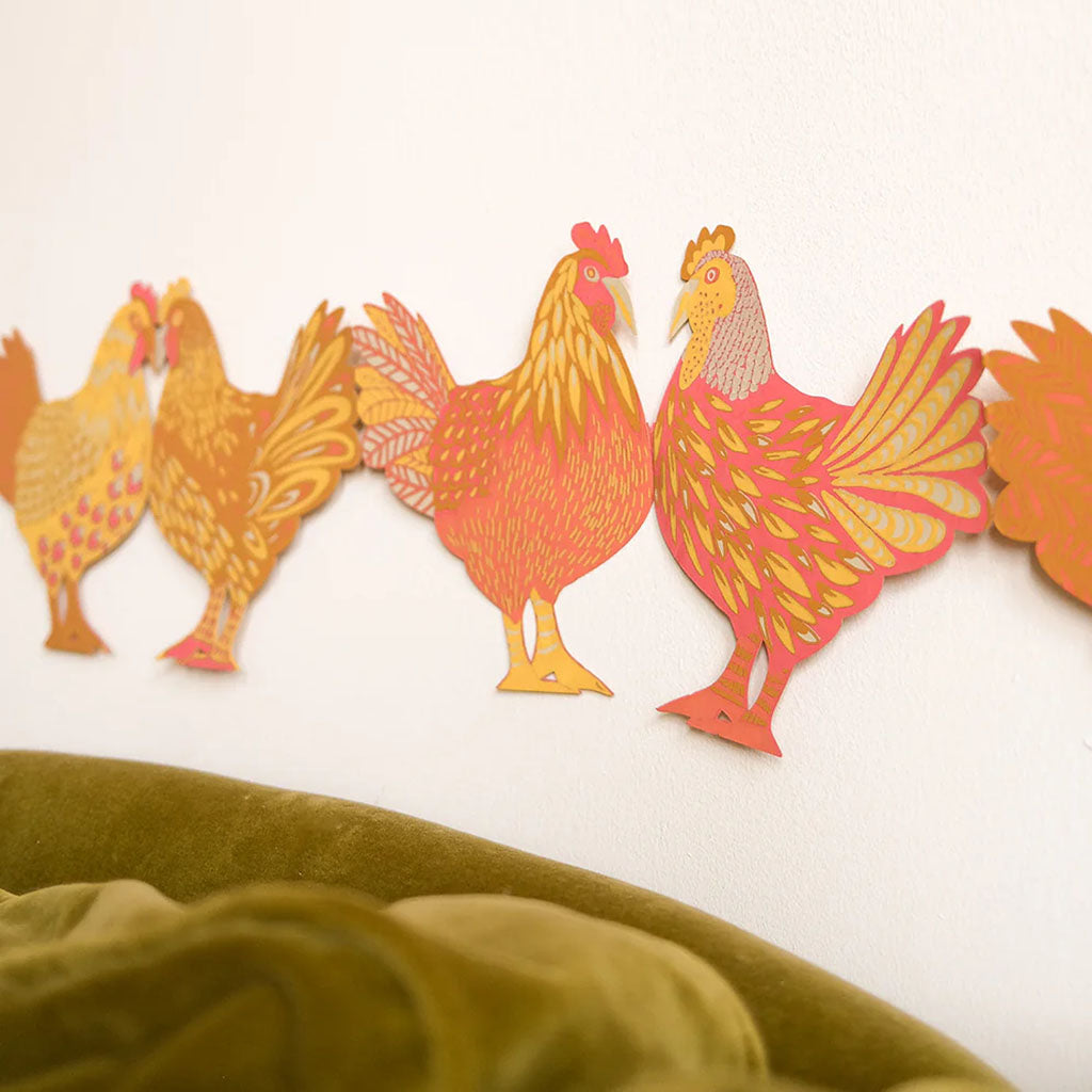 Decorative paper garland of chickens above a green sofa on a white wall