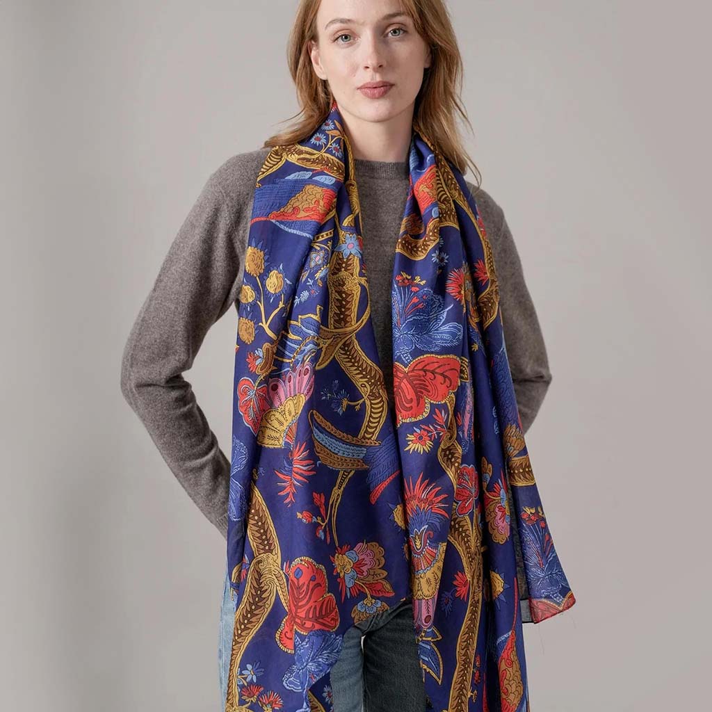 Woman wearing a colourful scarf with a peacock pattern on a plain background
