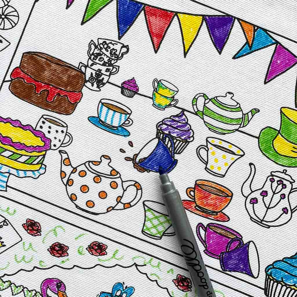 A close up image of one of the scenes from the back of a RBO Colour In Placemat. We can see various teapots and teacups, one of which has tipped over, and there are also various cakes and cupcakes visible. There is bunting along the top of the scene. Most of the individual elements have been coloured in, some fully and some still leaving some white areas, while the background is fully white. There is a blue pen in the foreground which is pointing to a blue coloured in teacup. 