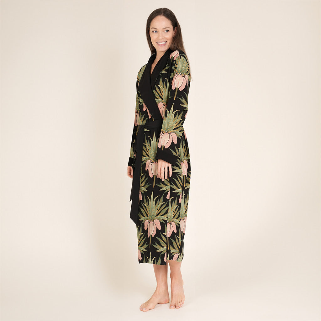 Woman wearing a black floral dressing gown with green leaf pattern on a beige background