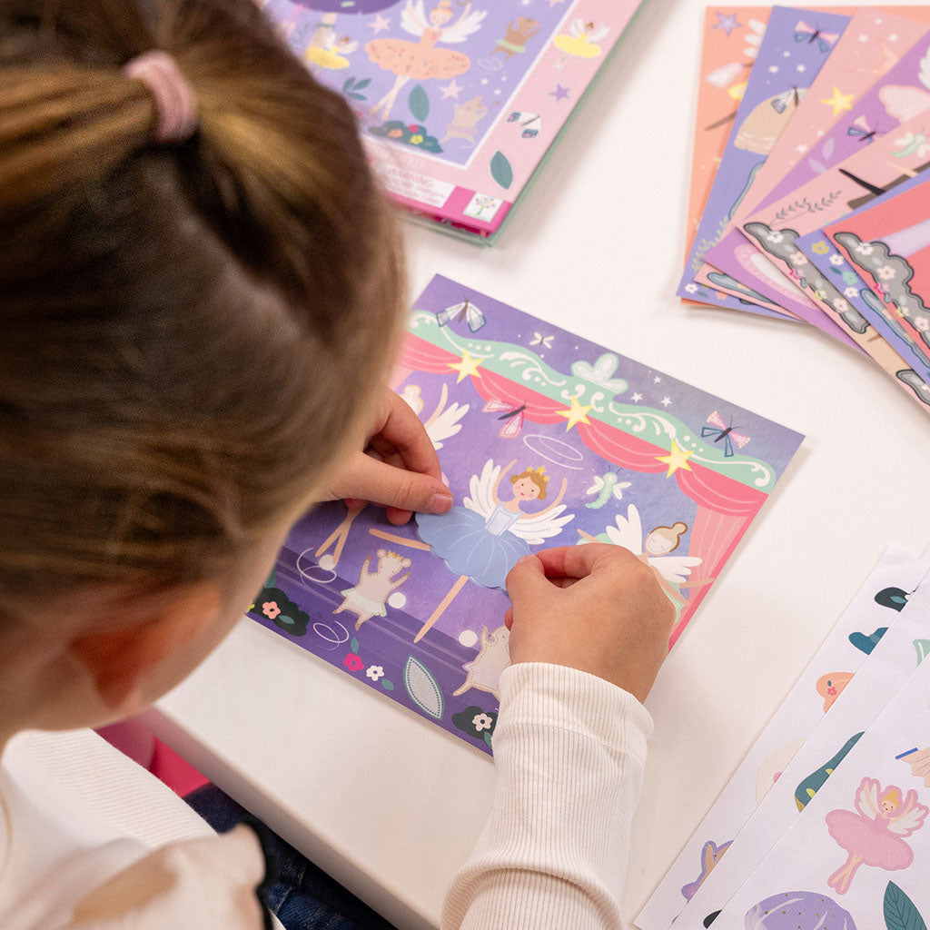 A child plays with the Enchanted Sticker Art book. Over her shoulder, we can see her placing a blue tutu onto a fairy. The fairy is on a purple background framed with red curtains and is surrounded by other fairies and dancing mice.