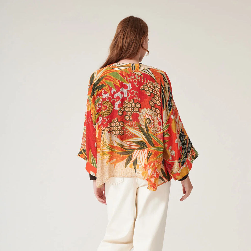 Back view of a woman wearing a colourful floral kimono-style top on a plain background