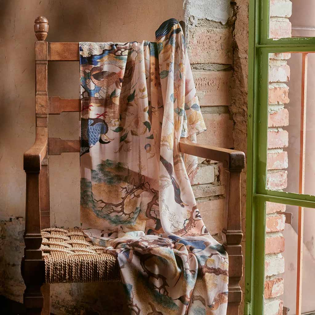 cream scarf with hummingbird illustration draped over a wooden chair next to a window with green frame