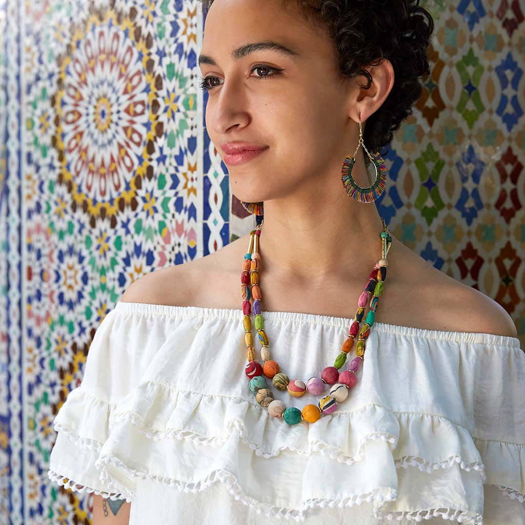 Woman wearing colourful kantha fabric necklace against a patterned wall
