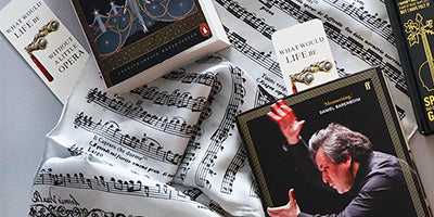 A styled flat-lay of music-themed items on a sheet music scarf, including a opera books and book marks