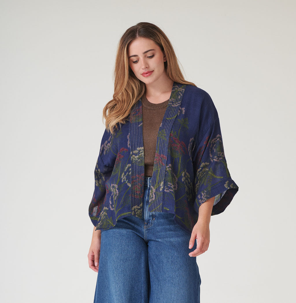 Woman wearing a blue seed wool kimono over a brown top and jeans on a white background