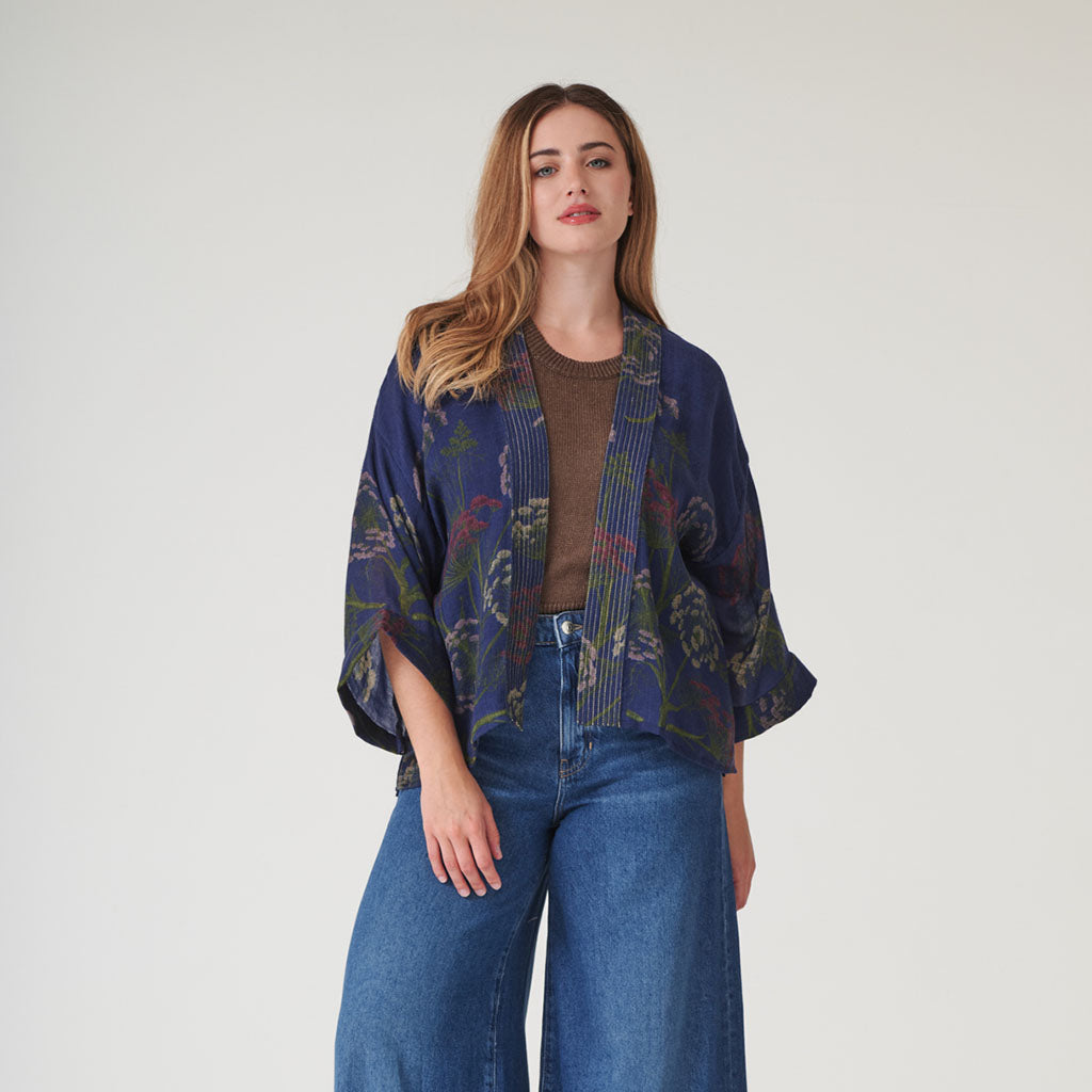 Woman wearing a dark blue patterned wool kimono over a brown top and blue jeans on a white background