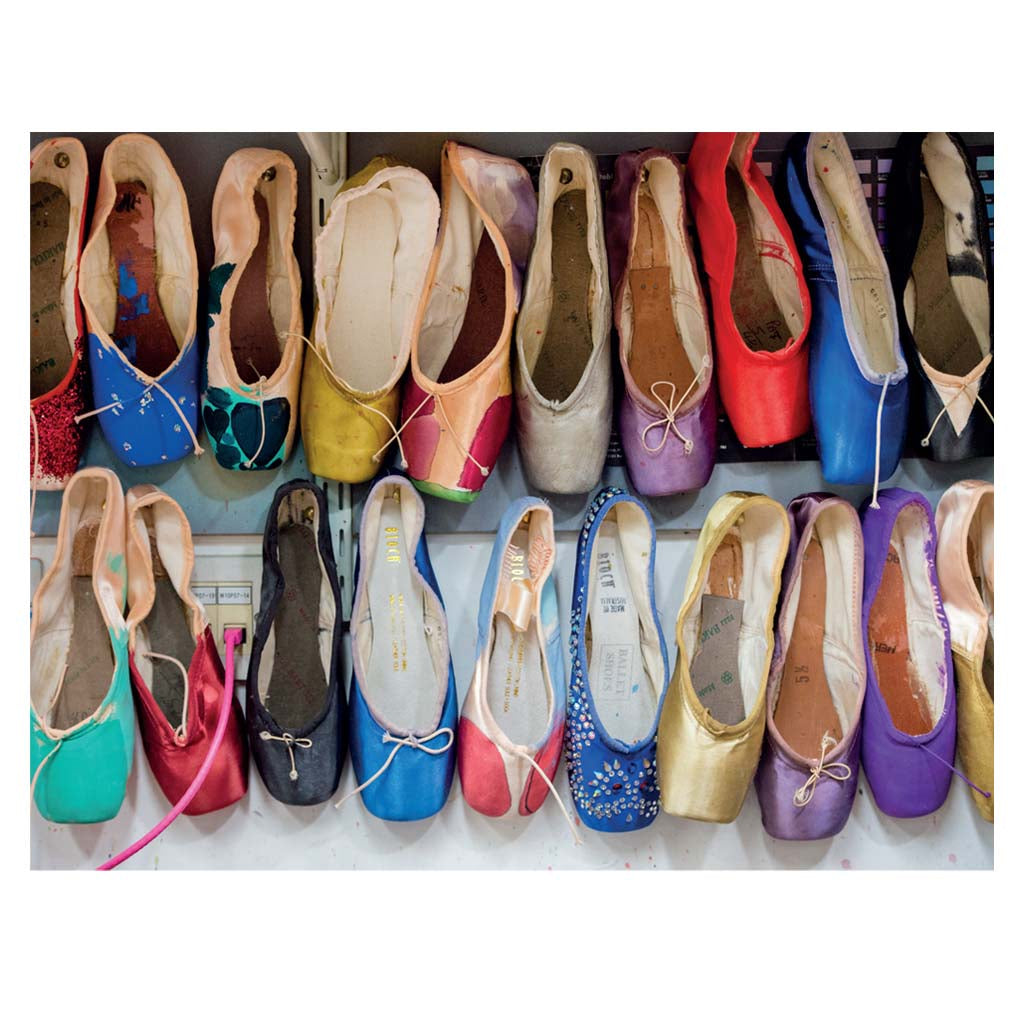 A selection of brightly coloured ballet pointe shoes in two rows of ten. They are in various colours and some have other embellishments such as bows or gems attached.