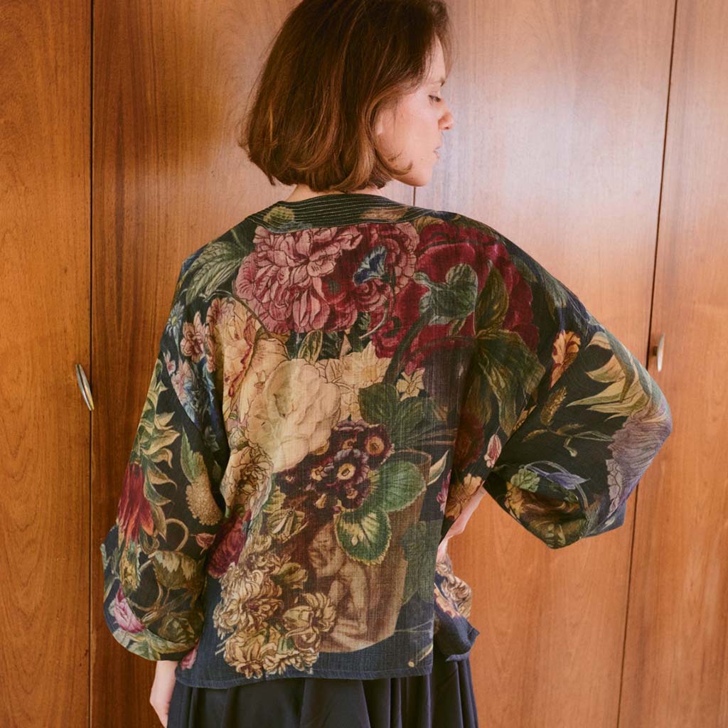 Person wearing a floral patterned kimono style jacket in front of a wooden door