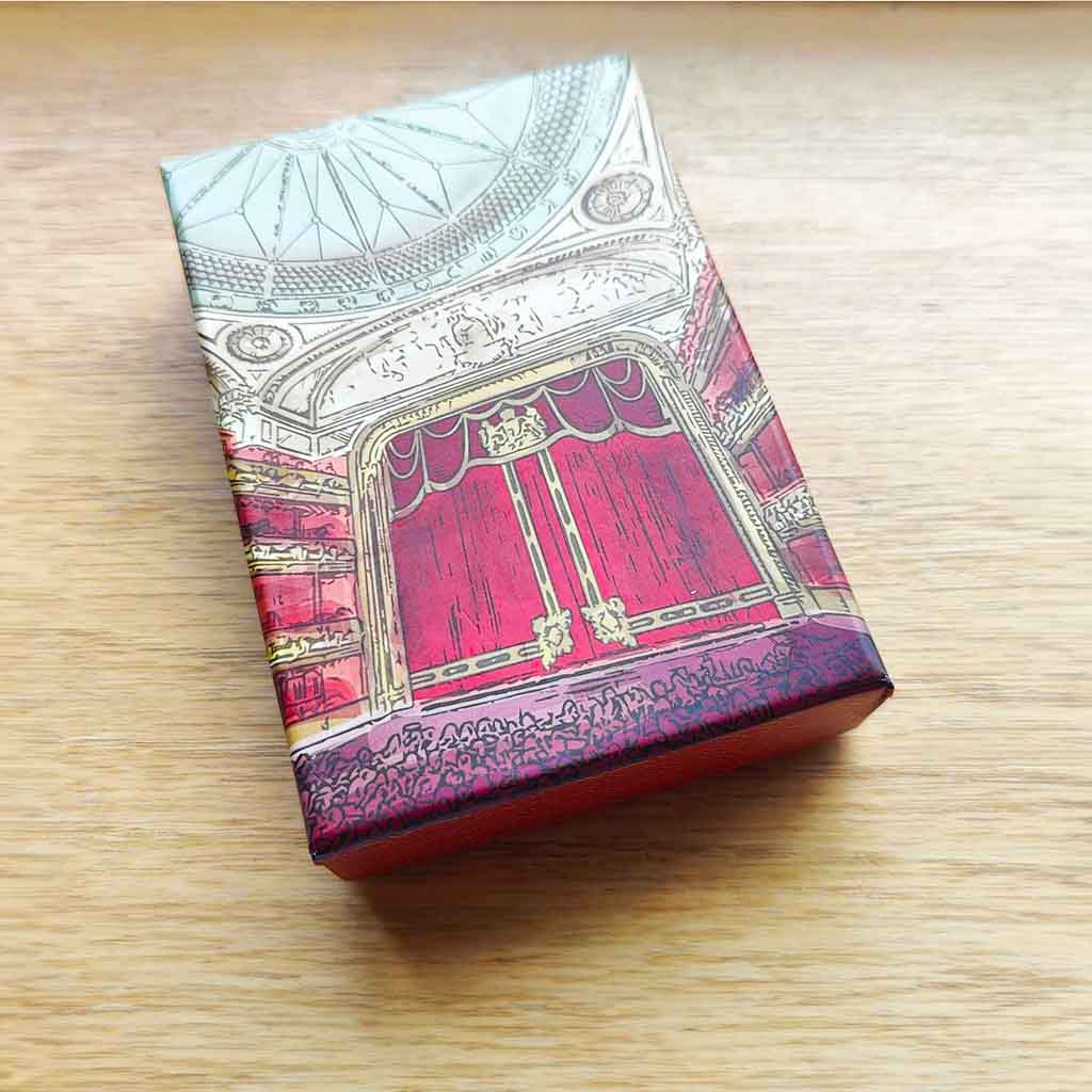 A close up of a box of Auditorium Playing Cards against a wood grain background. 