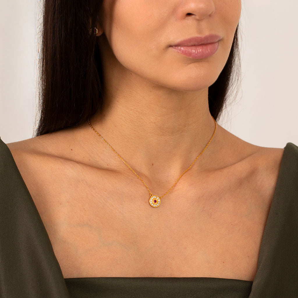 Woman wearing a gold necklace with a small round pendant against a neutral background