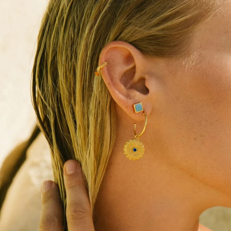 Close-up of a person wearing gold plated brass hoop earrings with a blue / navy gemstone.
