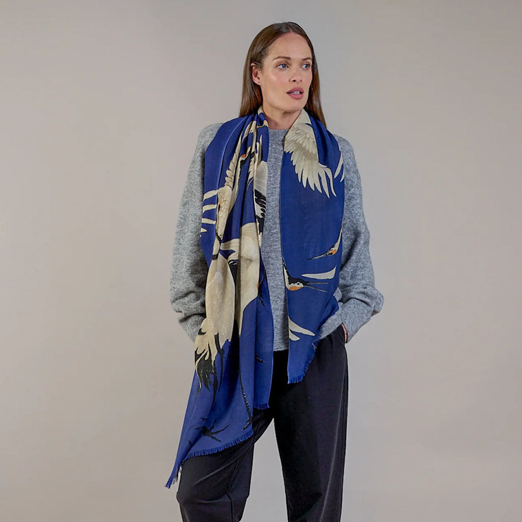 Woman wearing a blue scarf with stork design against a plain background