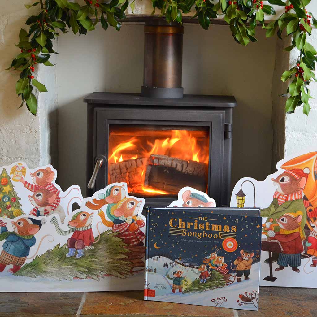The Christmas Songbook in front of a fireplace with cardboard cut outs of the books illustrations
