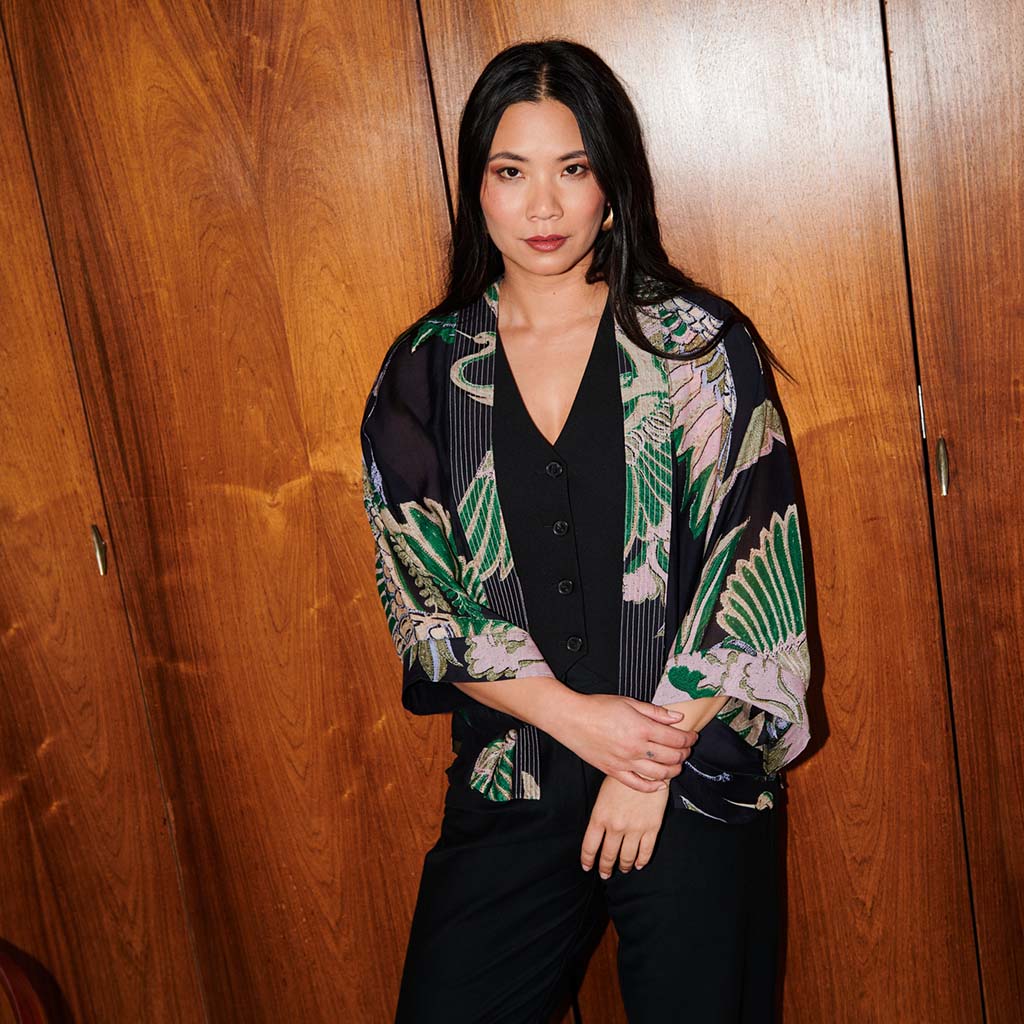 Woman wearing a crane patterned kimono style jacket in front of a wooden door