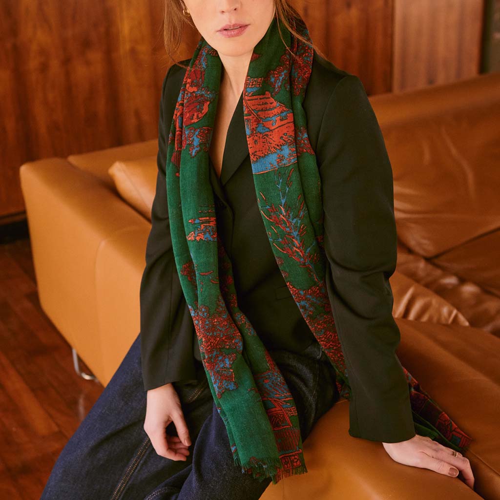 Person wearing a green and ref Pagoda Forest patterned scarf sitting on a brown leather couch.