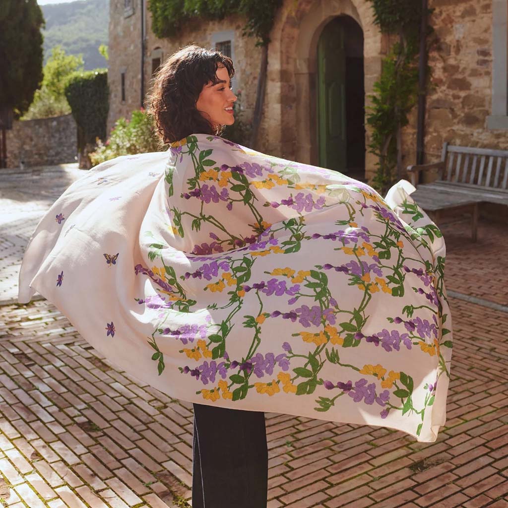 Woman holding a floral-patterned fabric outdoors in front of a stone building.