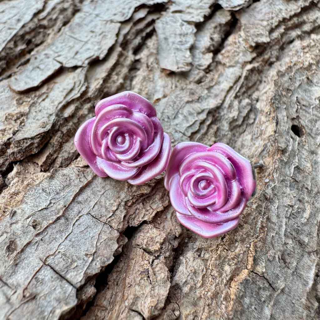 Pink rose-shaped earrings on a textured  tree bark surface