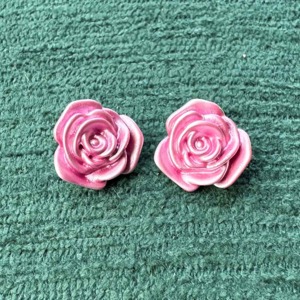 Pink rose-shaped earrings on a textured green surface