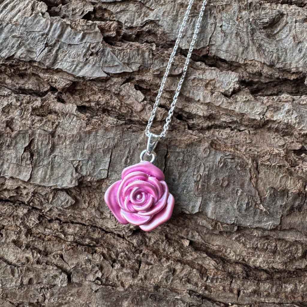 Pink rose-shaped pendant on a chain against a wooden background