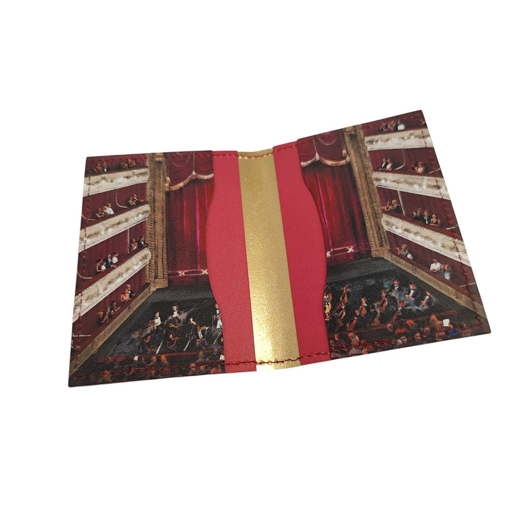 A leather card holder featuring a detailed illustration of the auditorium at the Royal Opera House with red curtains, balconies, and an orchestra. The centre of the wallet is accented with a vertical gold metallic stripe flanked by red panels.