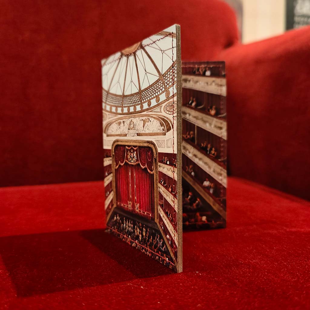 A leather card holder standing open on a red velvet surface, showing an interior view of the auditorium at the Royal Opera House with red curtains and tiered seating.