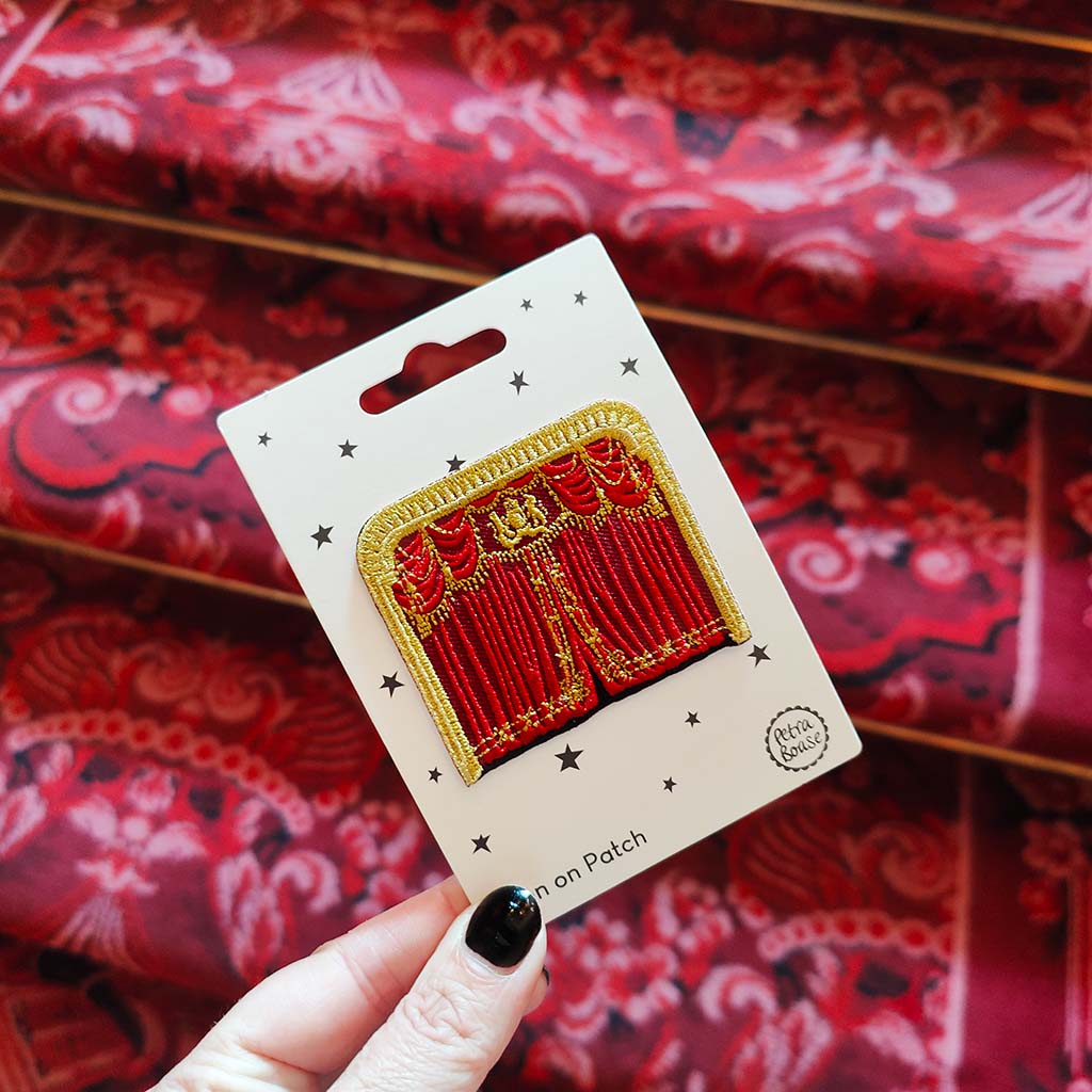 Red and gold theatre curtains embroidered patch on a card held over red fabric