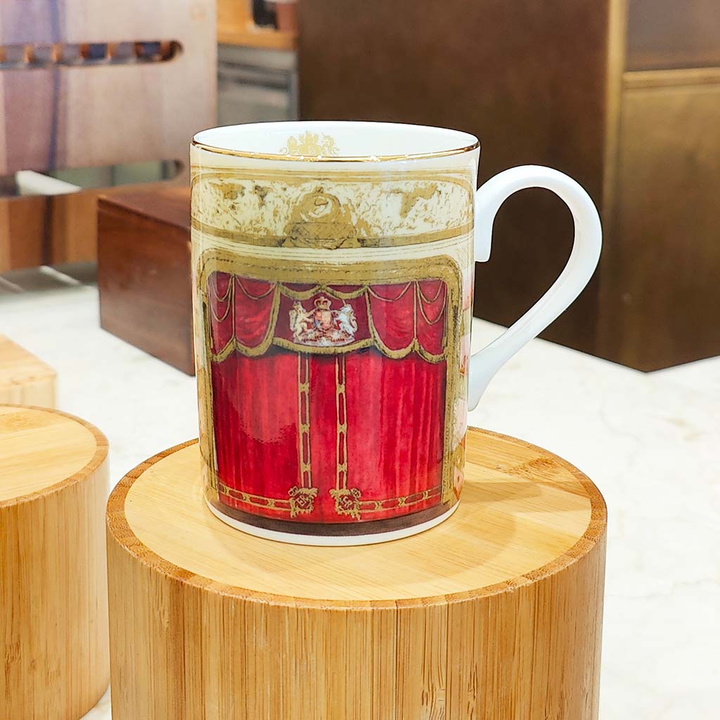 An Auditorium Mug sitting on a round wooden plinth. the background is out of focus but suggests that the mug is on display in some sort of shop environment. 