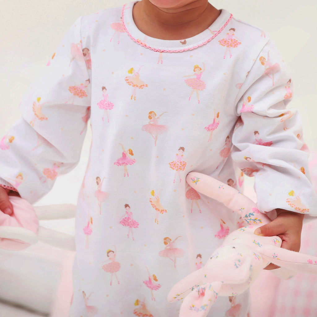Child wearing a white long-sleeve baby grow with pink ballerina print, holding a pink bunny toy.