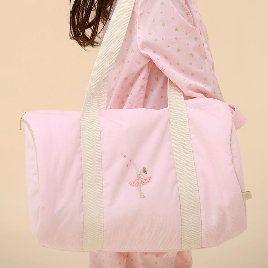 Pink  ballerina bag with cream straps held by a child wearing a pink pjs on a beige background