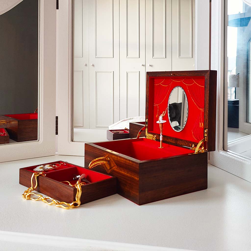 Wooden jewelry box with red interior and gold accents on a white floor.