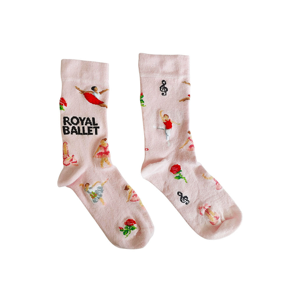 A pair of light pink socks featuring ballerina figures, musical notes, ballet shoes and flowers and the words 'ROYAL BALLET' in black text, displayed on a clean white background.