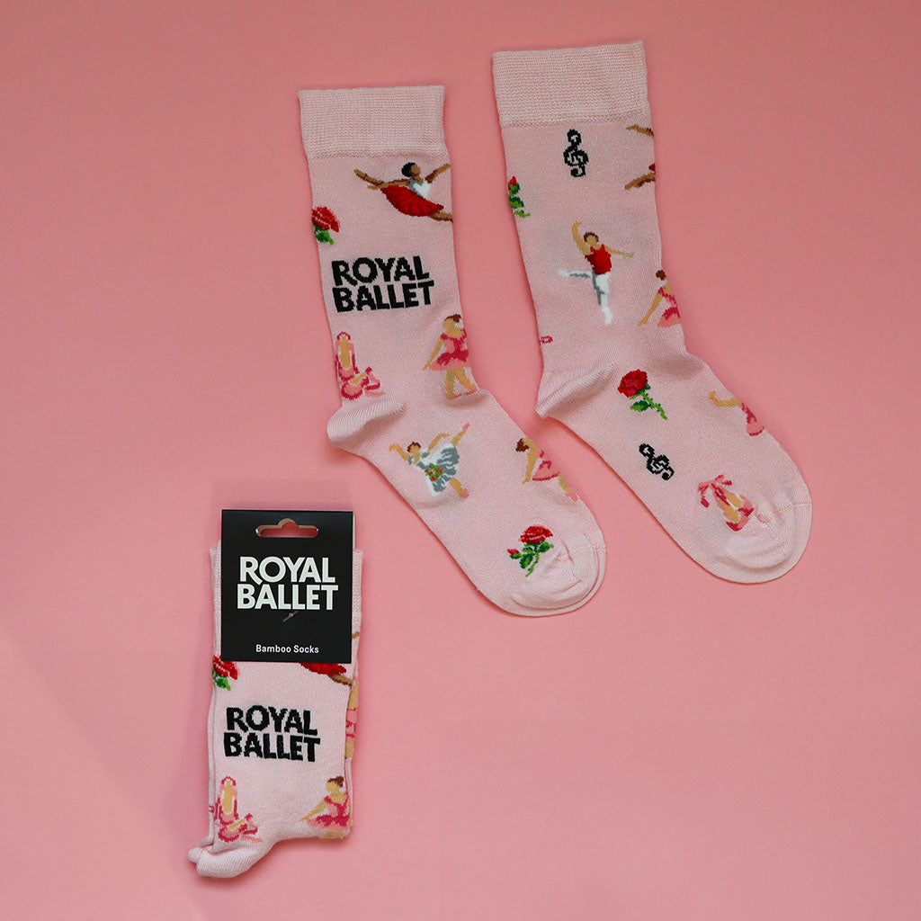 pink ballet socks featuring ballet dancers, roses, music notes, ballet shoes and black text 'ROYAL BALLET' on a pink background, one pair out of the packaging the other folded with a black cardboard label with ROYAL BALLET bamboo socks.