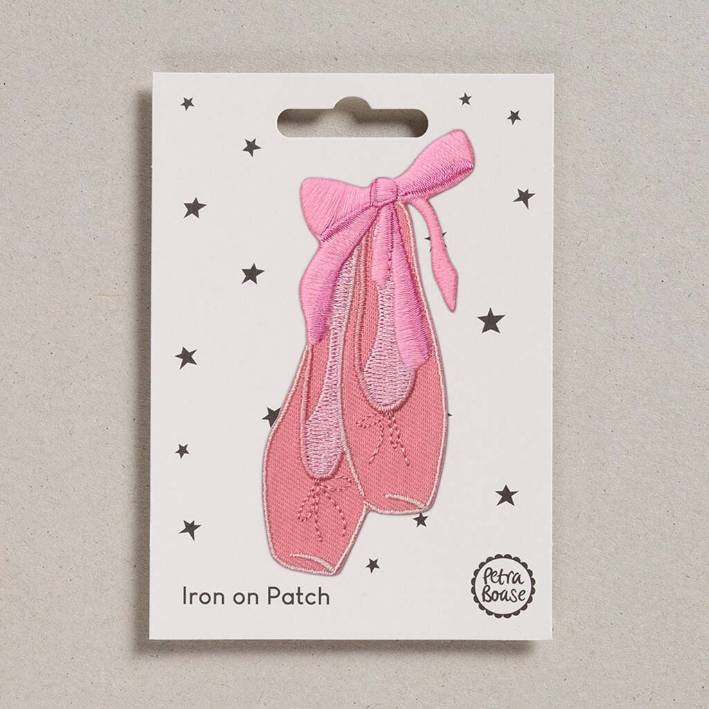Pink ballet shoe iron on patch with a bow on a white card with star patterns, branded 'Petra Boase'.