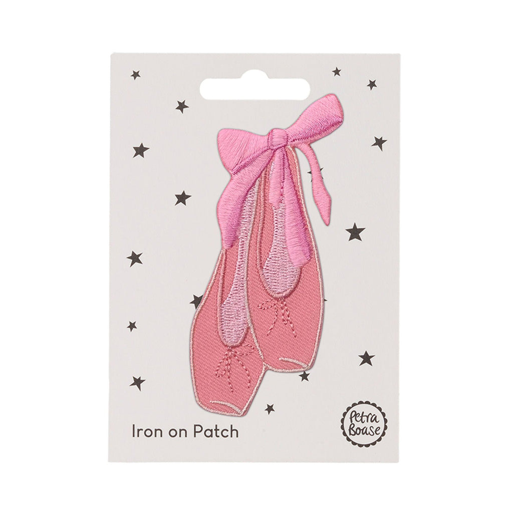 Pink ballet shoe iron on patch with a bow on a white card with star patterns, branded &#39;Petra Boase&#39;.