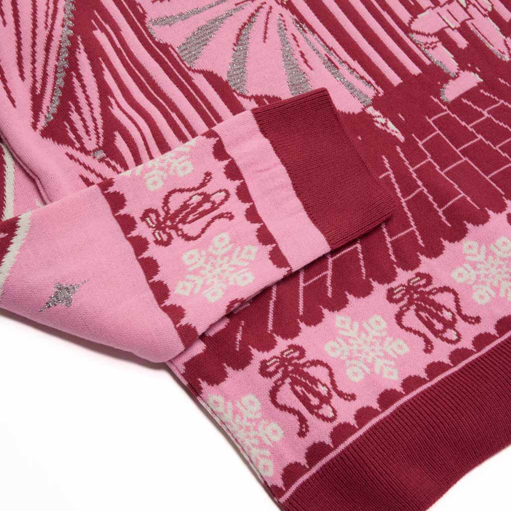 A close-up of a pink knit Barbie Royal Ballet Christmas Jumper with a dark pink graphic of a Clara and the Nutcracker on a stage, featuring patterned cuffs and hem.
